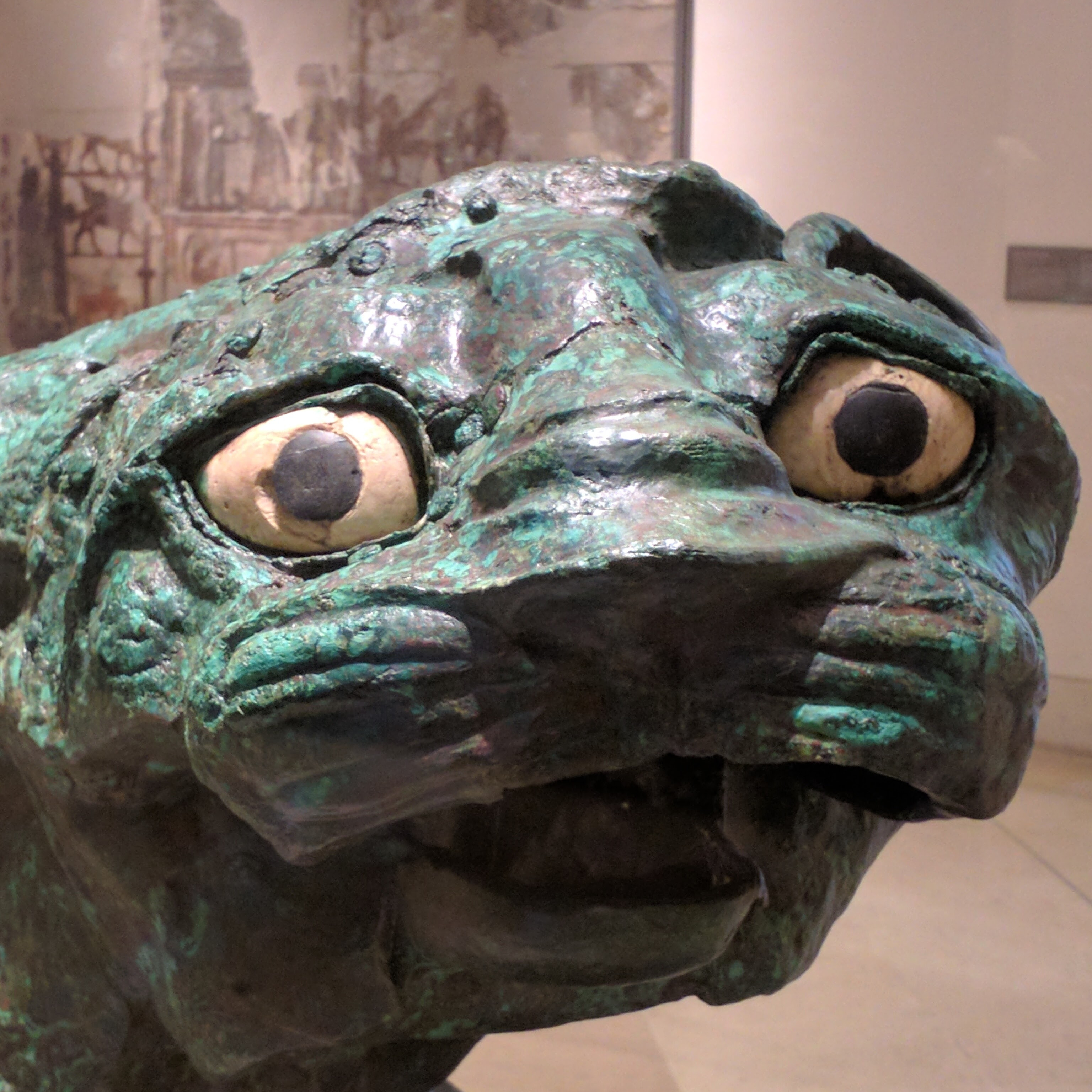 A
head-on picture of the Lion of Mari, a copper statue of a lion from Syrian
antiquity. It is green with wide, white eyes and small pupils. The mouth hangs
open in a goofy manner.