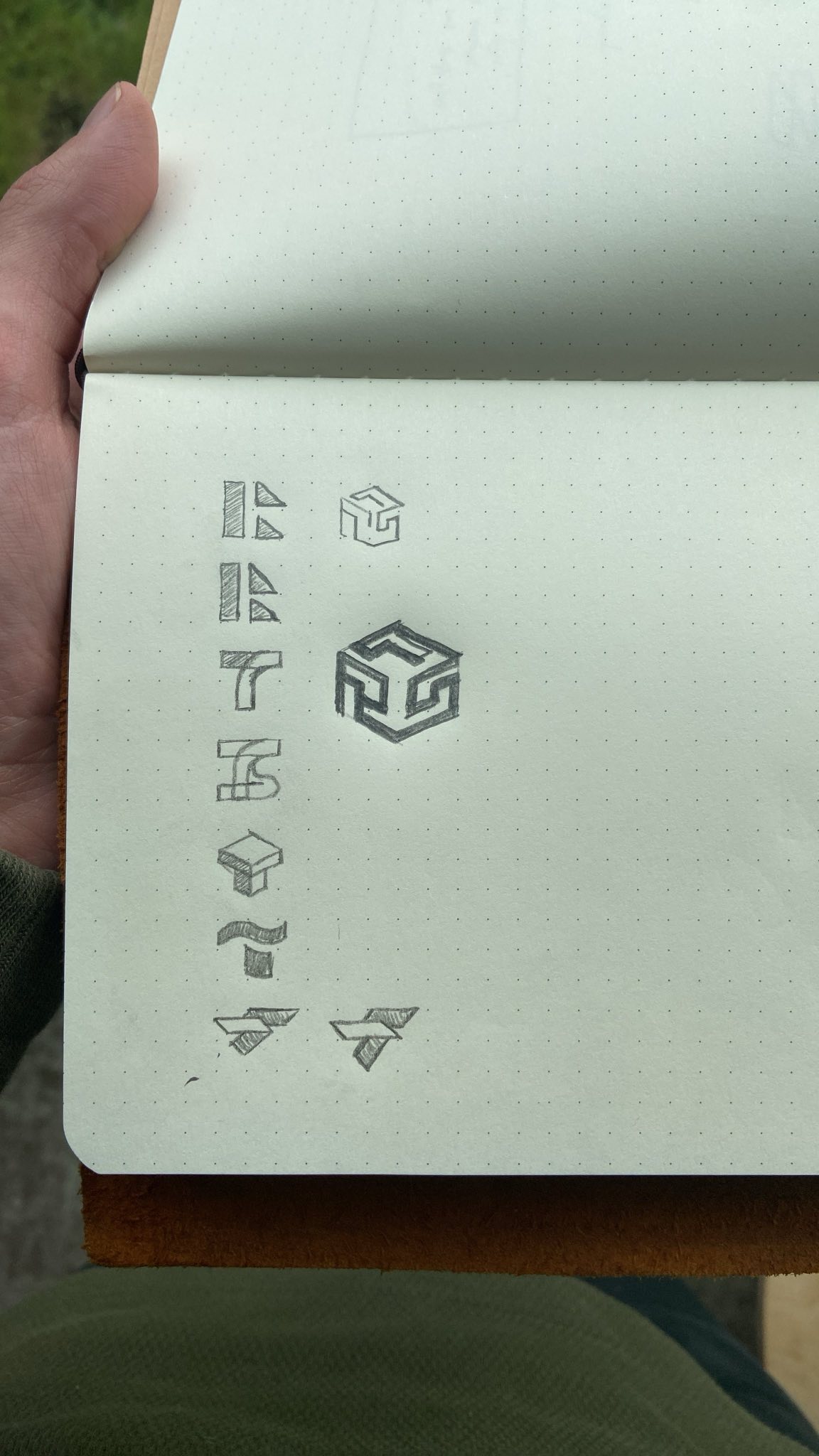 A top-down view of someone holding a dot-grid notebook with pencil
drawings of logos on the page. The logos are variations on the initials
RTS.